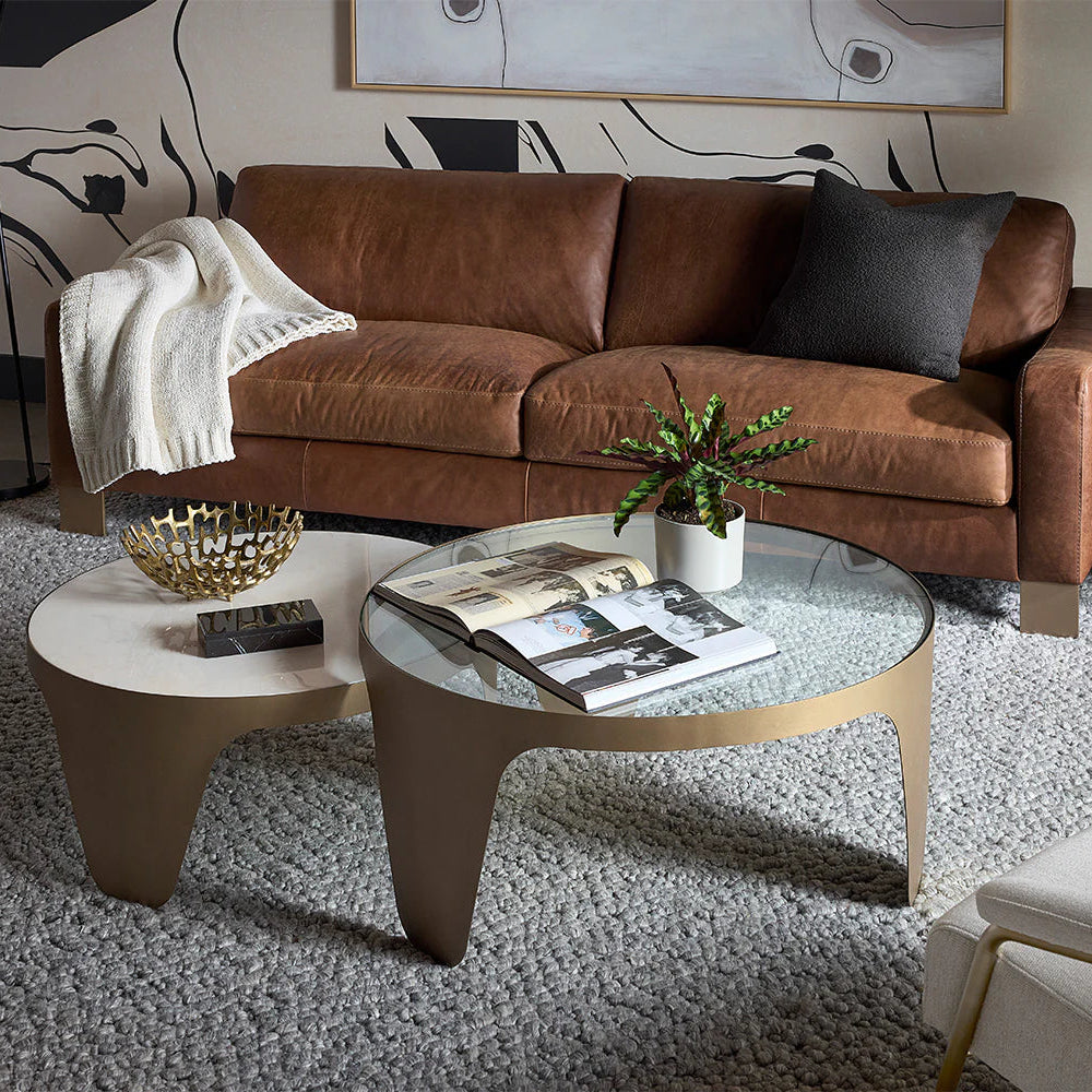 Modern living room with brown leather sofa, glass coffee table, and decorative elements.