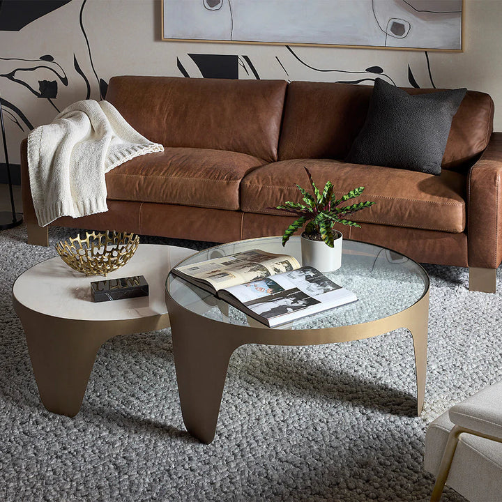Modern living room with brown leather sofa, glass coffee table, and decorative elements.