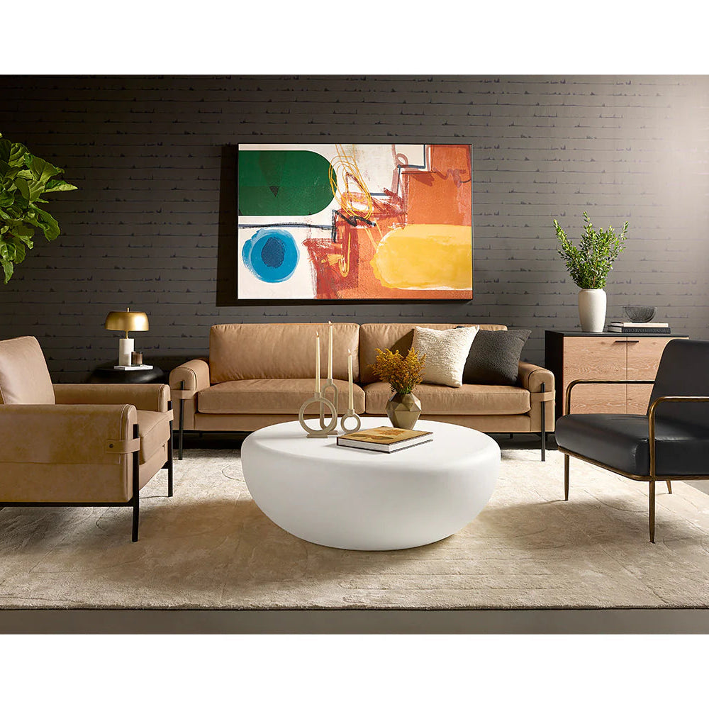 Modern living room with beige sofa, armchair, and black chair, white coffee table, and abstract painting on wall.