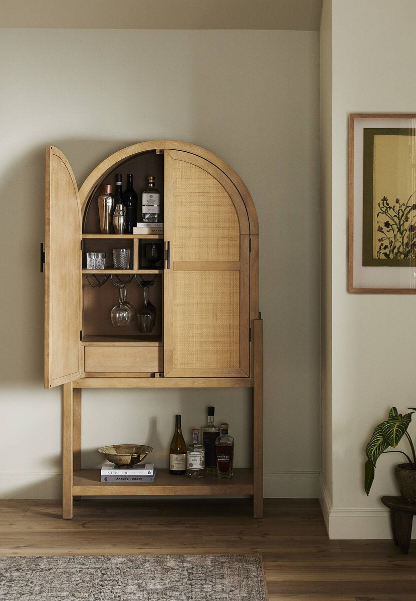 Wooden bar cabinet with open doors in a room with a plant and framed picture on the wall.
