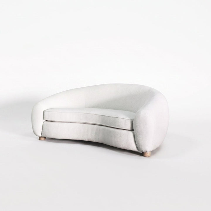 A modern curved lounge chair upholstered in a light off-white fabric, shown on a seamless white studio background.