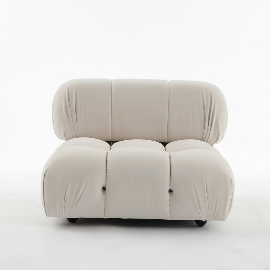 A modern modular upholstered lounge chair in a warm off-white or cream fabric, featuring a low, rounded, segmented design, photographed against a plain white studio background.