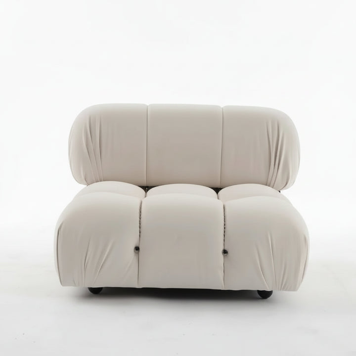 A modern modular upholstered lounge chair in a warm off-white or cream fabric, featuring a low, rounded, segmented design, photographed against a plain white studio background.