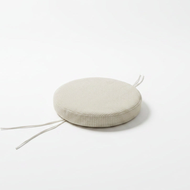 A round woven floor cushion in a light beige color with white tie straps