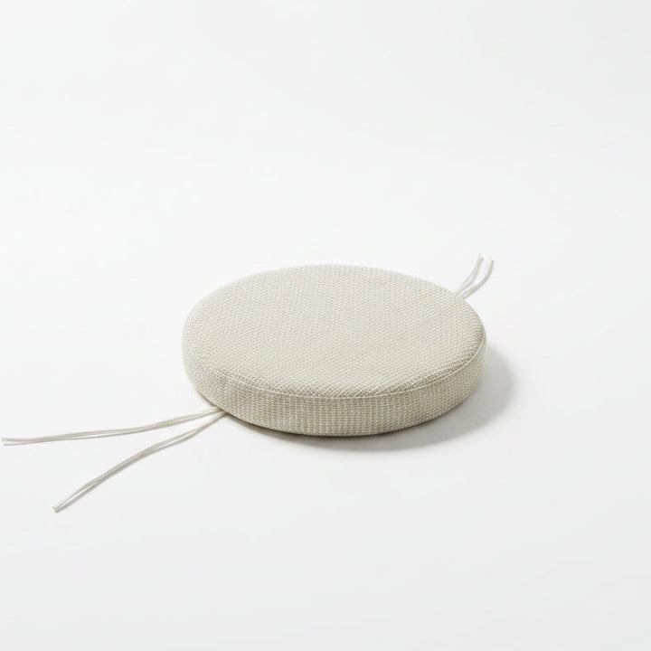 A round woven floor cushion in a light beige color with white tie straps