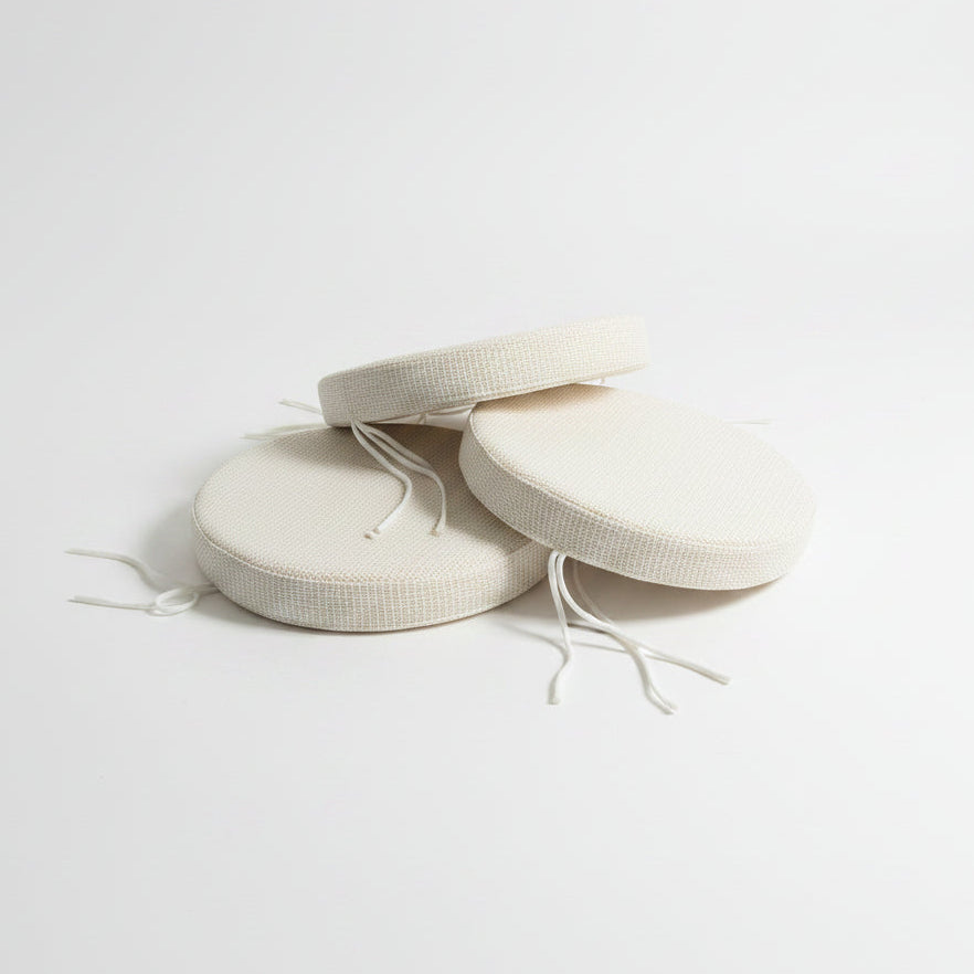 Three round off-white woven seat cushions with white drawstrings, stacked on a white background