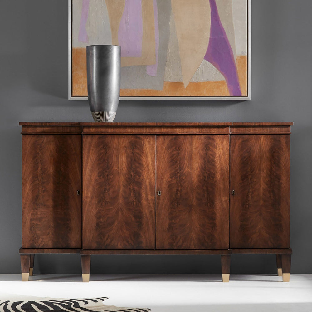 A mid-century modern wooden credenza or sideboard with four doors, rich brown burl wood grain, and light-colored tapered legs, styled in a room setting with a silver vase and a framed abstract painting on a gray wall.