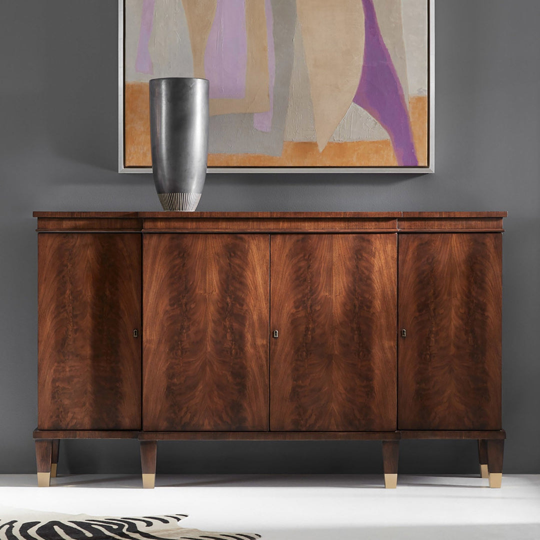 A mid-century modern wooden credenza or sideboard with four doors, rich brown burl wood grain, and light-colored tapered legs, styled in a room setting with a silver vase and a framed abstract painting on a gray wall.