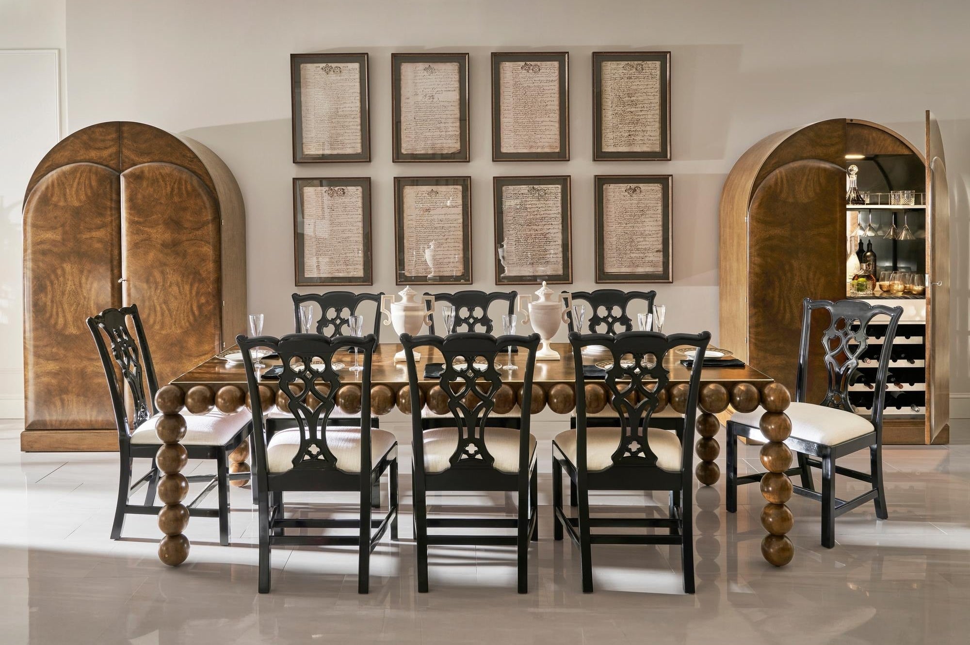 Dining room with wooden table and chairs, framed pictures on the wall, and arched wooden doors.