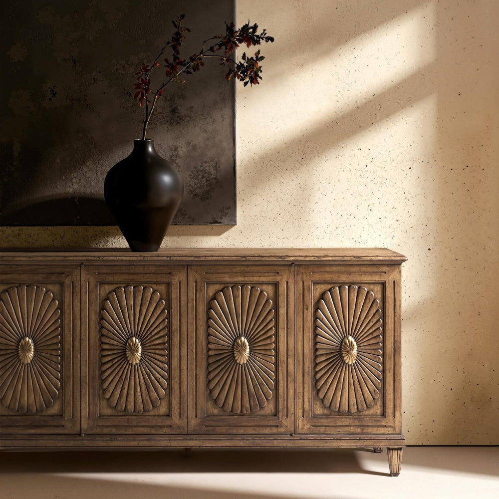 Wooden sideboard with decorative carvings in a room with a textured wall and vase.