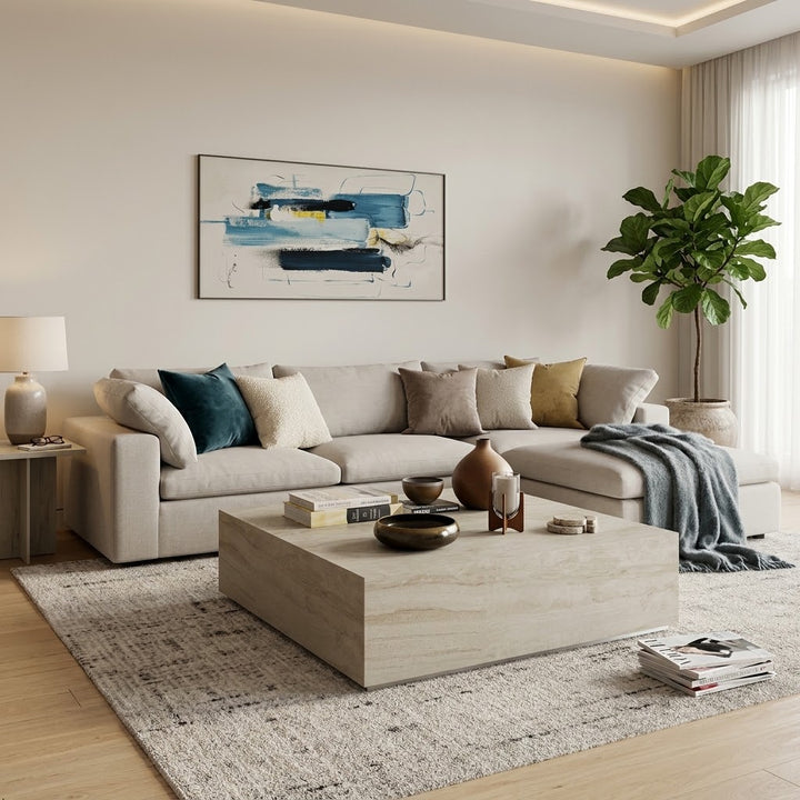 A modern living room featuring a light beige sectional sofa with neutral and blue accent pillows, a large rectangular light wood coffee table, a textured gray area rug, and a framed abstract blue and black painting on the wall.